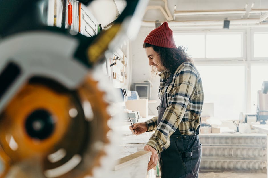Focused carpenter measuring wood in a well-lit workshop, utilizing a miter saw.